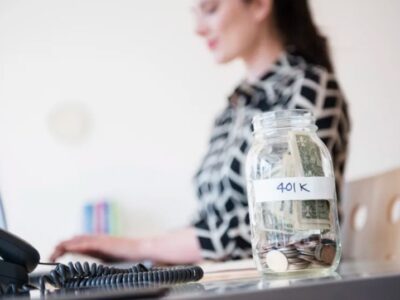 A person using a computer and a glass jar full of money