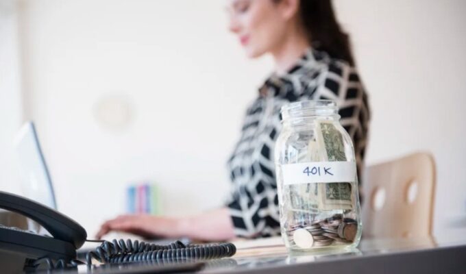 A person using a computer and a glass jar full of money